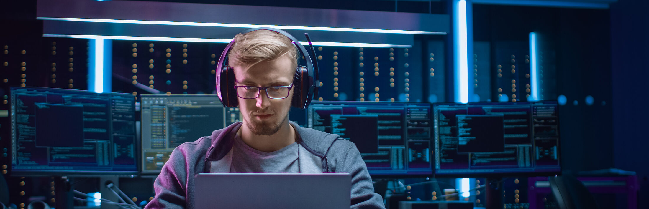Mann mit Brille und Kopfhörern bedient mit Maus Labtop in einer Computer Zentrale