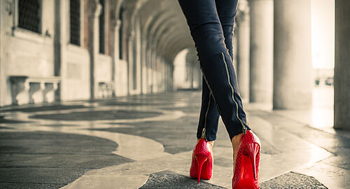 Frau mit roten Schuhen läuft Säulengalerie entlang