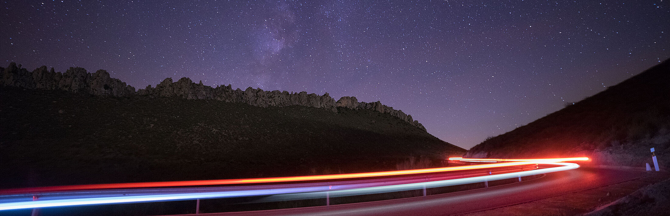 Langzeitbelichtung von Straße bei Nacht mit Sternenhimmel und Wald im Hintergrund